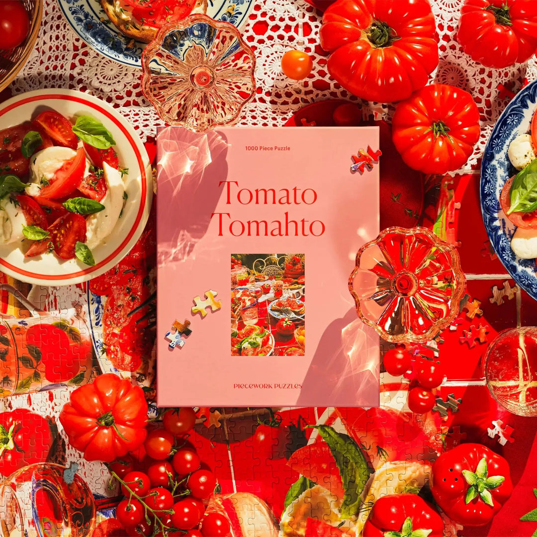 Pink 'Tomato Tomahto' puzzle box surrounded by fresh tomatoes and tomato-themed food on a decorative tablecloth.