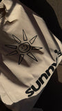 A cream-colored canvas tote bag with a black hand-drawn sun graphic and the 'sunny's' printed in black, shown in dramatic natural sunlight on concrete.