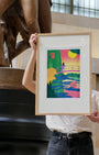 Person holding a framed colorful artwork in front of a statue