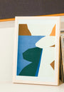 Framed abstract art print with geometric shapes on a shelf.
