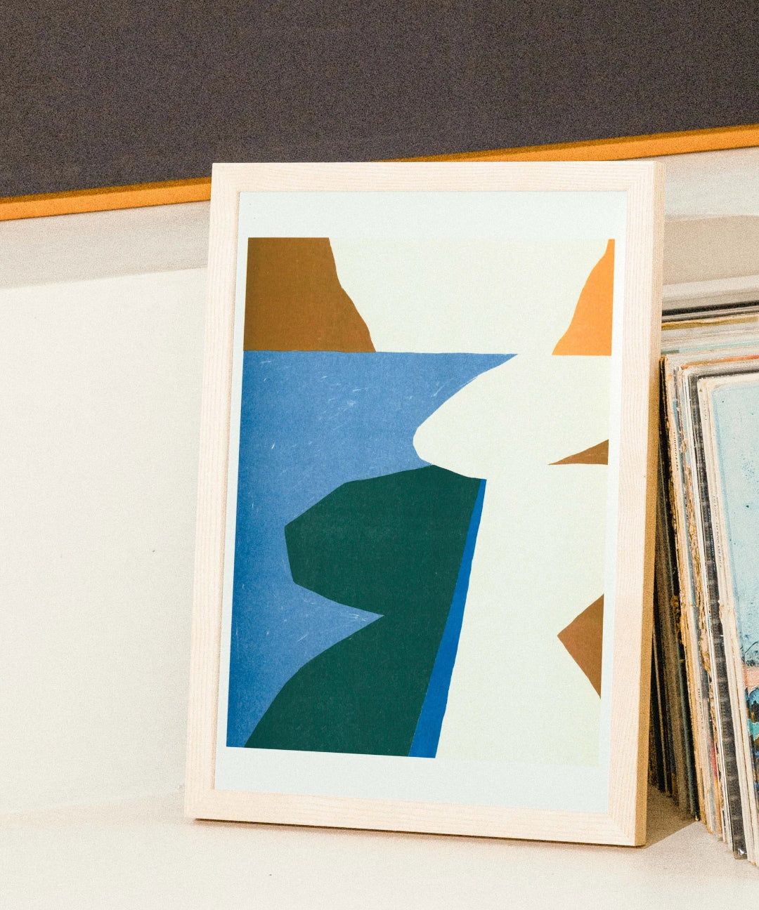 Framed abstract art print with geometric shapes on a shelf.