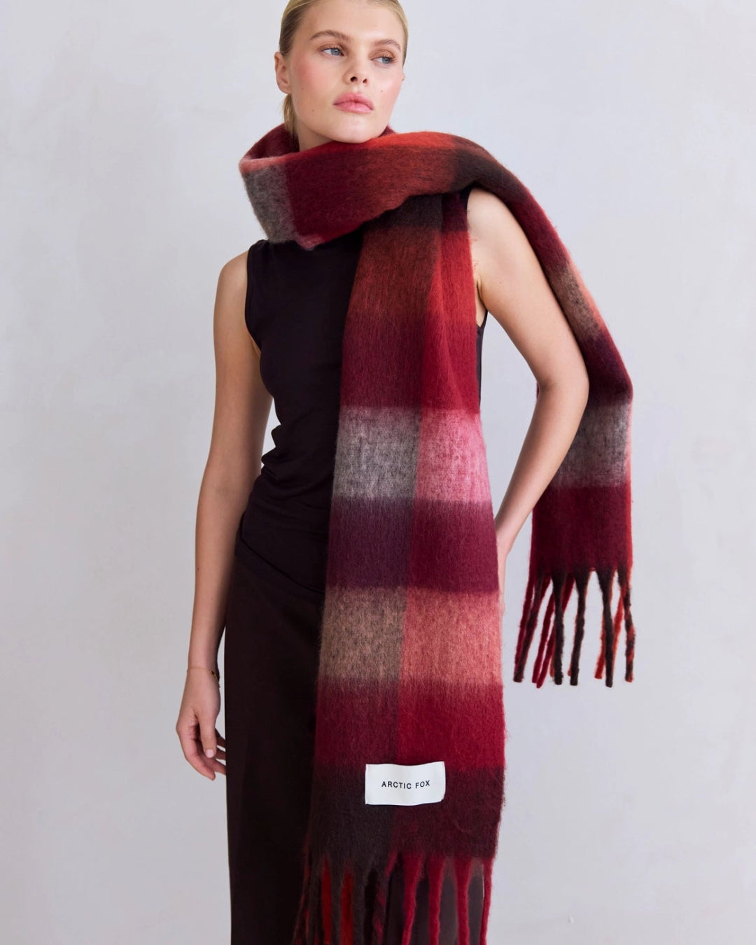 Model wearing a red and brown checkered scarf with a visible brand label on a light gray background