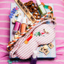 Colorful items including a striped bag, nail polish, and snacks on a pink and white striped background.